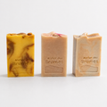 Trois savons rectangulaires, au dessus texturé et portant le logo Atelier des Brumes en relief, sur un fond blanc.  À gauche, savon Orange + Géranium, de couleur jaune et orange marbré.  Au centre, savon Sauge + Camomille, de couleur rose pâle.  À droite, savon Ylang-ylang + Litsée citronnée. 