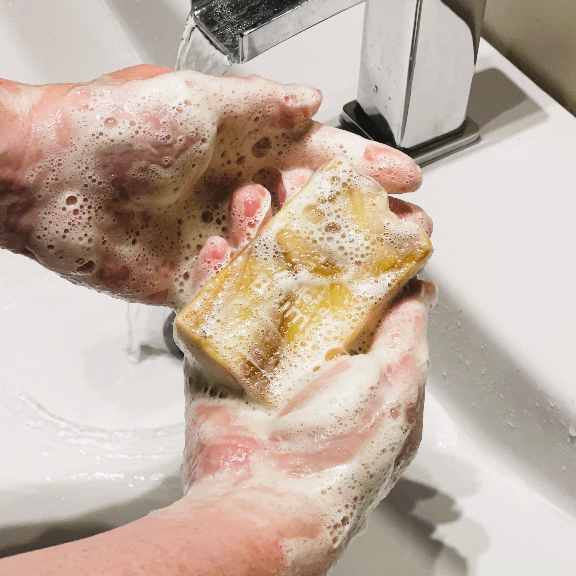Mains et savon couverts de mousse au dessus d'un lavabo