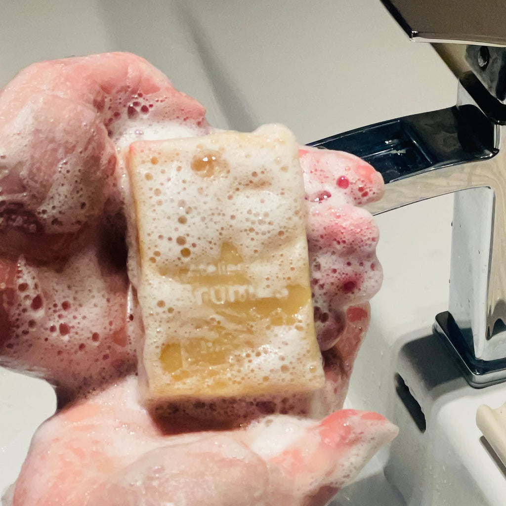 mains couvertes de mousse tenant un savon au dessus d'un lavabo