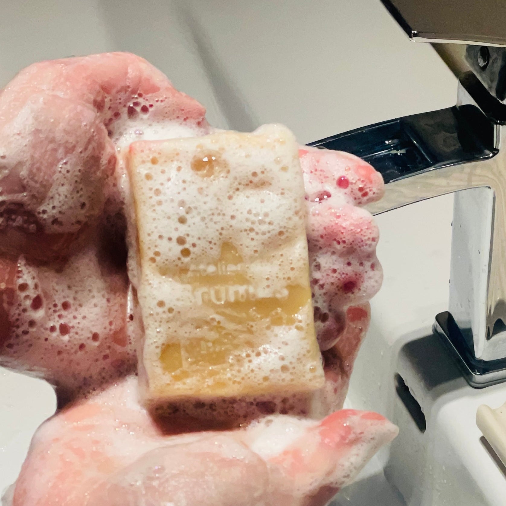 mains couvertes de mousse tenant un savon au dessus d'un lavabo