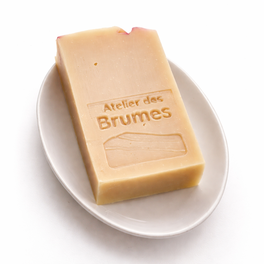Savon Sauge + Camomille, de forme rectangulaire, de couleur rose pâle avec un logo Atelier des Brumes en relief.  Déposé à plat sur un porte-savon ovale. 