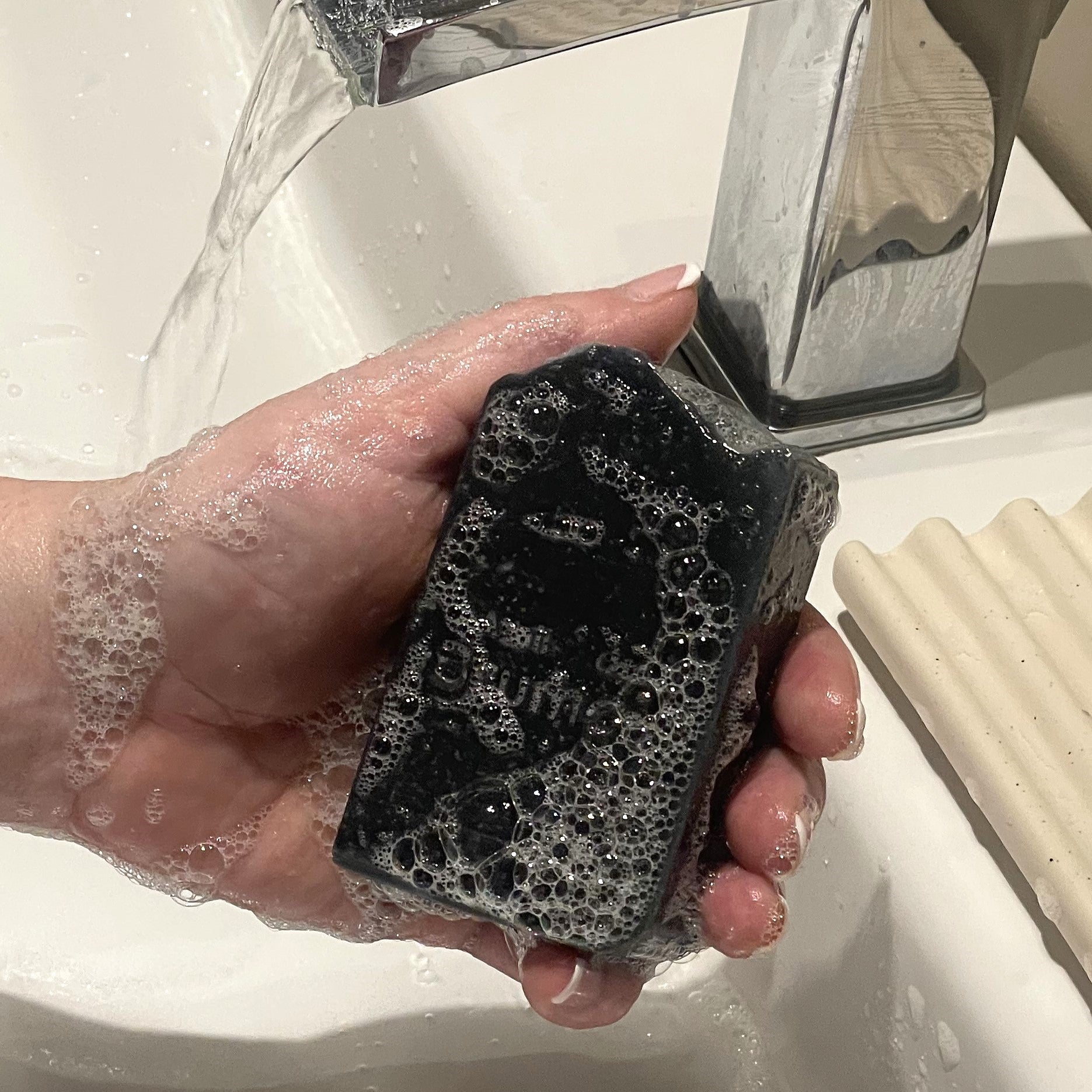 main qui tient un savon noir avec mousse au dessus d'un lavabo