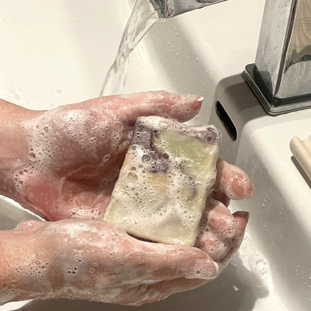 mains qui tiennent un savon couvert de mousse près d'un lavabo