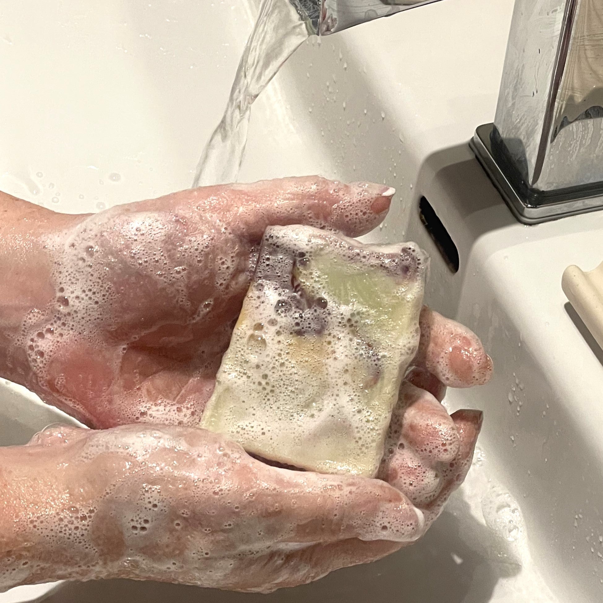mains qui tiennent un savon couvert de mousse près d'un lavabo