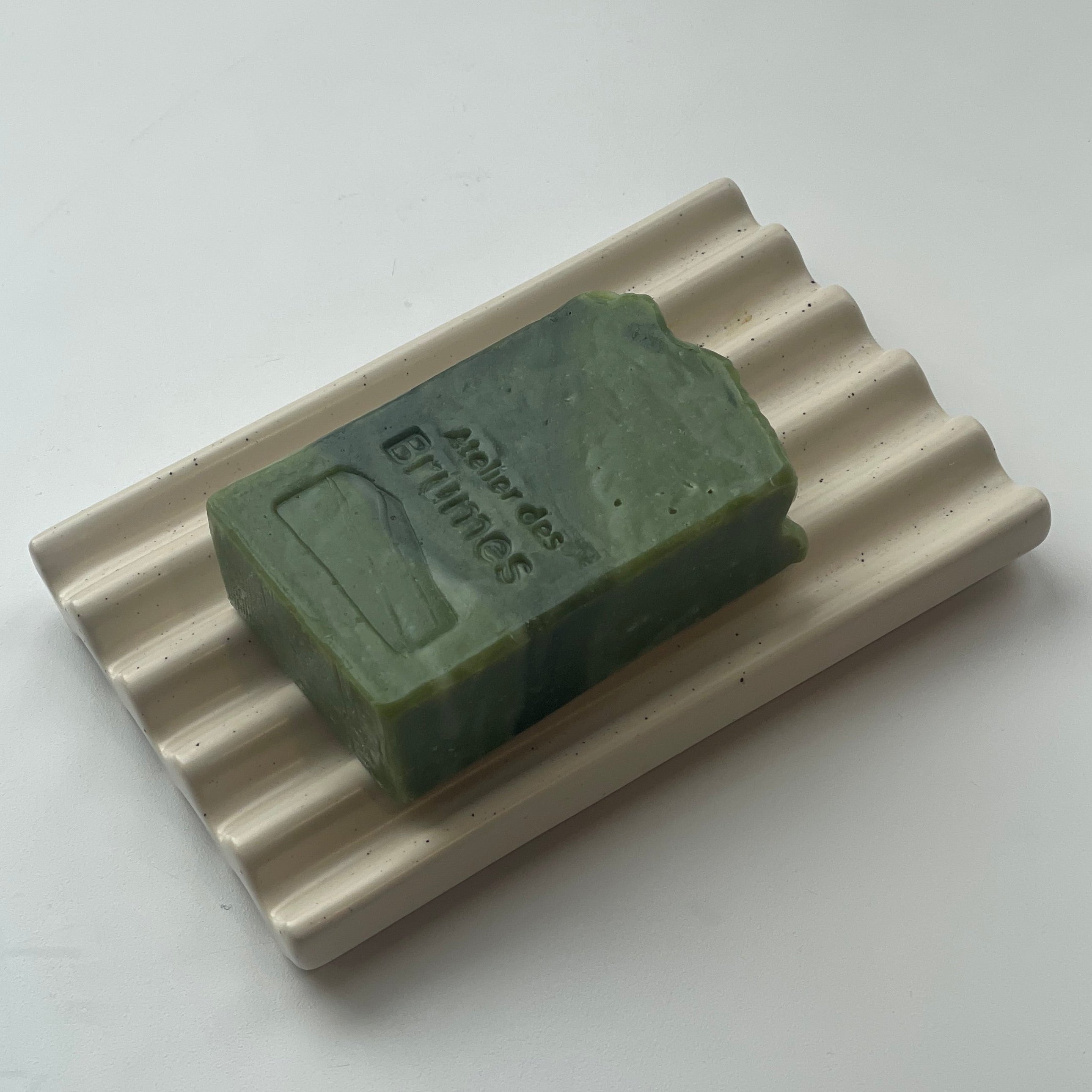 savon rectangulaire vert avec une bande noire sur un porte-savon beige