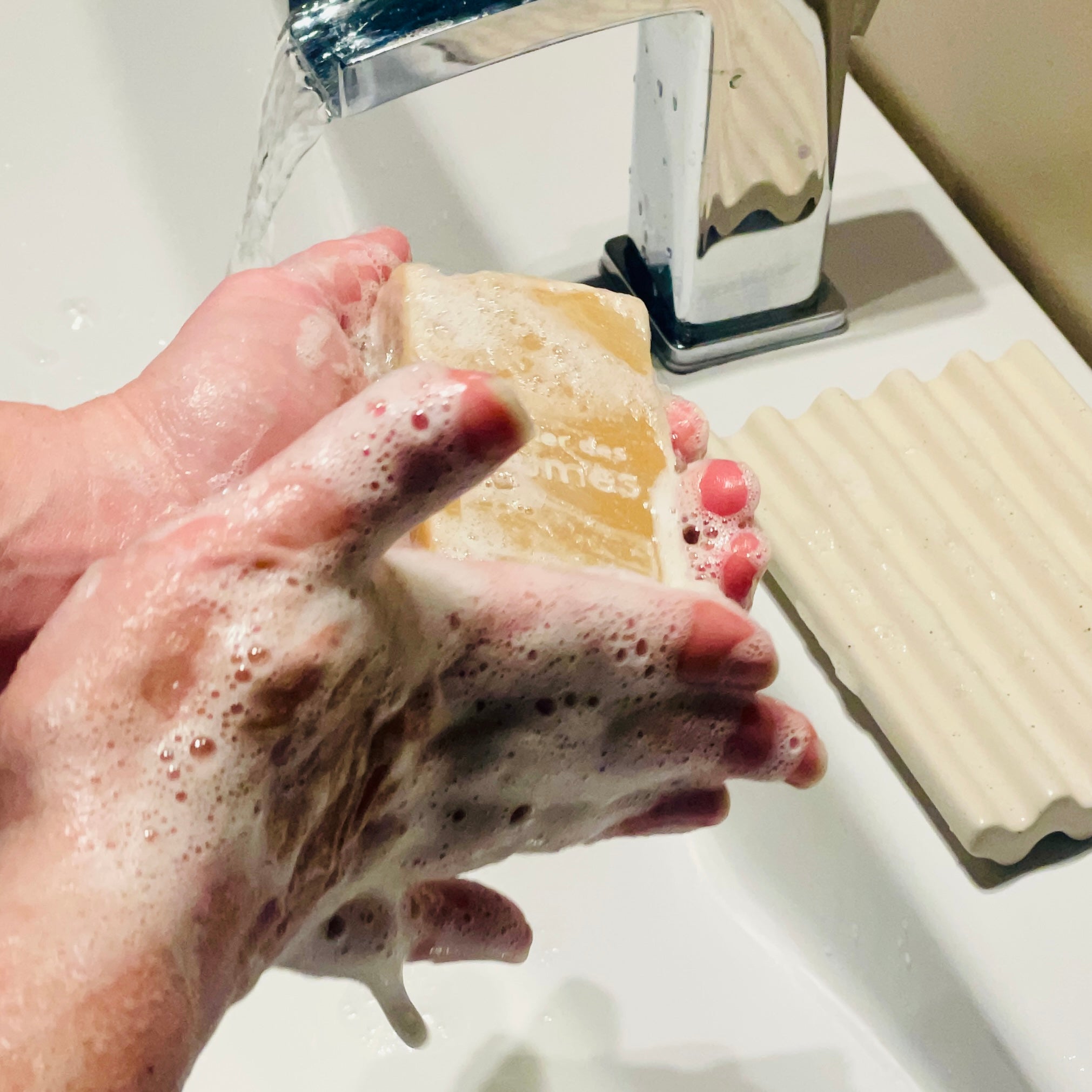 deux mains couvertes de mousse tenant un savon au dessus d'un lavabo
