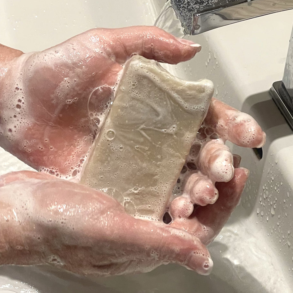 mains qui tiennent un savon rectangulaire crème couvert de mousse au dessus d'un lavabo